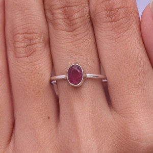 May include: A silver ring with a red oval gemstone. The ring is on a finger.