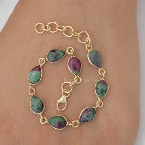 May include: Gold chain bracelet featuring teardrop-shaped green and pink gemstones. The bracelet has a lobster clasp fastening.