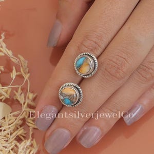 May include: A pair of round stud earrings with a silver-colored rope design border. Each earring features a turquoise and tan stone. The earrings are displayed on a hand with a neutral-colored nail polish. The text "ElegantsilverjewelCo" is visible.