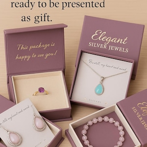 May include: Four mauve jewelry boxes containing a gold ring with a purple stone, a silver necklace with a turquoise teardrop pendant, silver earrings with pink teardrop stones, and a pink beaded bracelet, all featuring the text Elegant SILVER JEWELS.