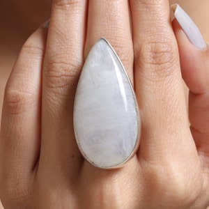 Puede incluir: Un anillo en forma de lágrima con una piedra de luna blanca engastada en plata.