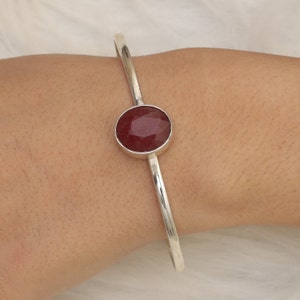 Peut inclure: Un bracelet jonc en argent avec une pierre précieuse ronde rouge sertie au centre.