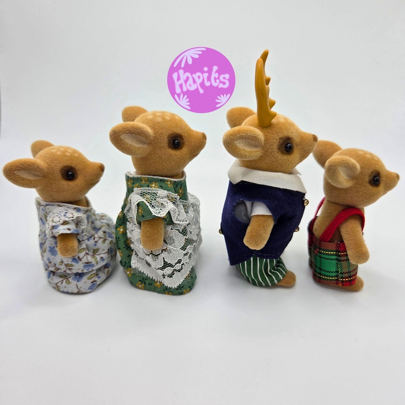 May include: Four fawn-colored deer figurines. One wears a floral dress, another a green dress with lace, a third a blue vest and striped pants, and the last a plaid overall. The image includes a purple circle with the text "Hapits".