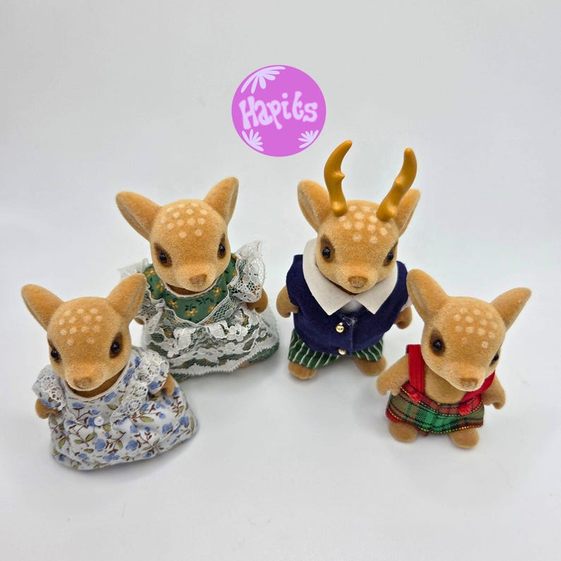 May include: Four fawn-colored deer figurines with white spots. Two deer wear floral dresses, one wears a navy blue jacket with green striped pants, and one wears a red and green plaid outfit. The image includes a purple circle with the text "Hapits".