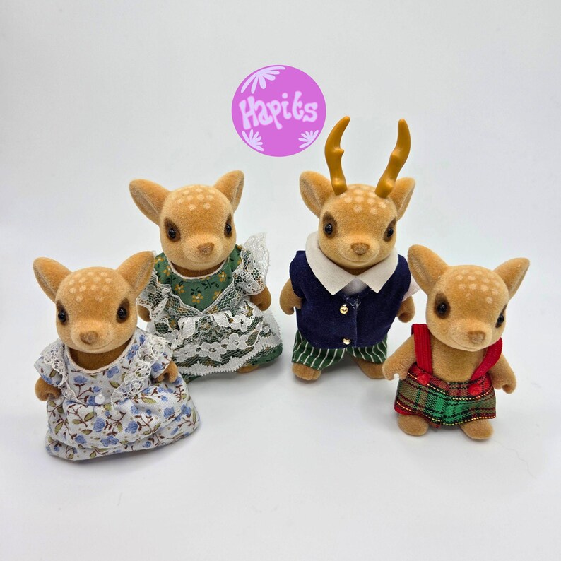 May include: Four fawn-colored deer figurines, each with a unique outfit. One wears a floral dress, another a green dress with lace, a third a navy vest and striped pants, and the last a plaid overall. A purple circle with the text "Hapits" is in the background.