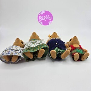 May include: Four miniature toy animal figures, each wearing different outfits. One wears a blue floral dress, another a green dress with white lace, a third a navy blue jacket and green striped pants, and the last a red and green plaid dress.