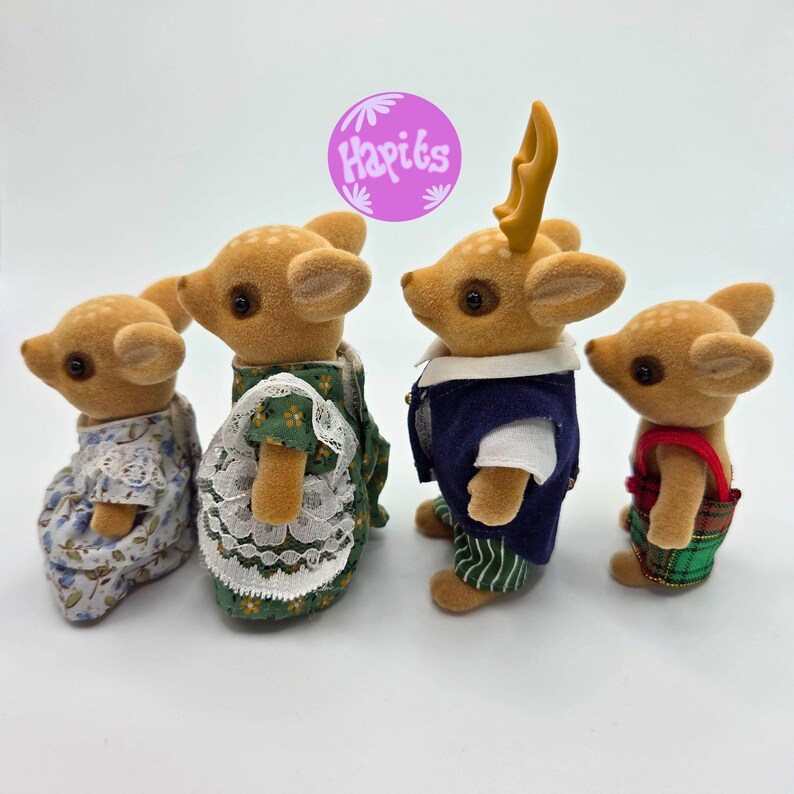 May include: Four miniature deer figurines, each with a unique outfit. The deer have brown fur and are wearing dresses, vests, and overalls. One deer has yellow antlers. The image includes a purple circle with the text "Hapiks".