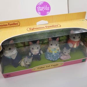 May include: A Sylvanian Families Fisher Cat Family toy set in a clear plastic box. The set includes five figures: a father, mother, son, daughter, and a baby. The figures are all gray and white with black stripes. The box is pink and white with the words "Sylvanian Families" and "Fisher Cat Family" printed on it.