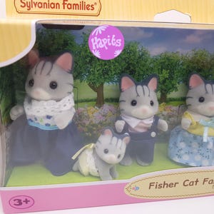 May include: A family of four gray and white tabby cats from the Sylvanian Families toy line. The family includes a mother, father, and two children. The mother is wearing a blue dress with a white lace collar and a floral pattern. The father is wearing a blue jumpsuit with a white collar. The children are wearing a blue and white dress and a gray and white jumpsuit. The box has the text "Fisher Cat Family" and "Sylvanian Families" on it.