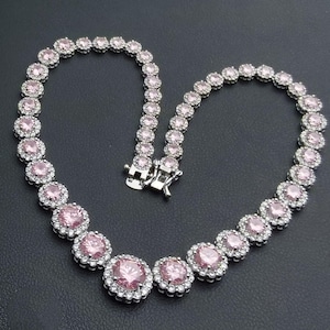 Op de afbeelding: Een zilverkleurige ketting met roze edelstenen en heldere accentstenen. De ketting is in een hartvorm gerangschikt tegen een zwarte achtergrond. De sluiting is zilver.