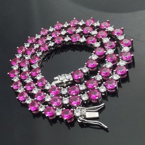 Può includere: Una collana a catena d'argento con pietre rotonde rosa. La catena è realizzata con piccoli anelli rotondi ed è composta da due file di pietre.