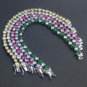 May include: A multi-colored gemstone bracelet with yellow, pink, green, and blue stones. The bracelet is made of silver-colored metal and has a clasp closure. The gemstones are arranged in rows.