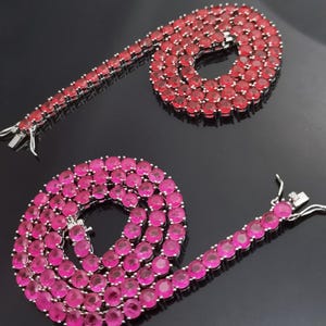 Puede incluir: Dos cadenas de plata con piedras redondas rojas y rosas. Las cadenas son de plata y tienen un cierre de broche.