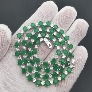 May include: A silver chain necklace with alternating green and white round stones.