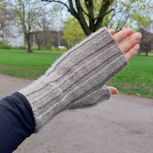 Könnte beinhalten: Nahaufnahme eines grauen, gestrickten Fingerlosen Handschuhs mit Rippenstruktur. Der Handschuh wird an der Hand einer Person getragen, die Finger sind ausgestreckt.