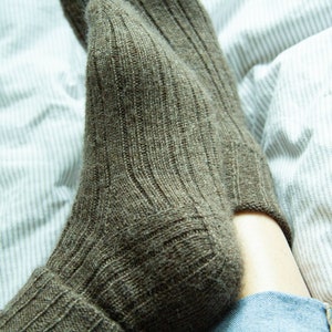 May include: A pair of brown wool socks with a ribbed texture. The socks are folded down at the top and are being worn by a person.
