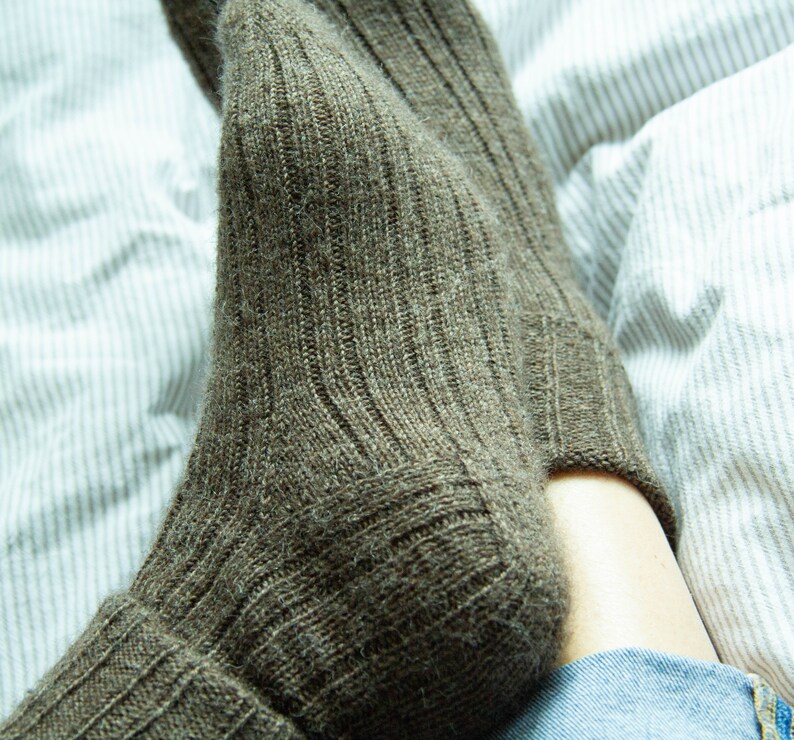 May include: A pair of brown wool socks with a ribbed texture. The socks are folded down at the top and are being worn by a person.