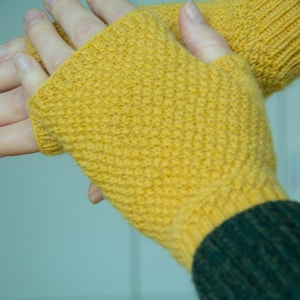 Op de afbeelding: Een paar gele vingerloze handschoenen met een textuur in gebreid patroon. De handschoenen zijn gemaakt van een zacht, warm materiaal en perfect om je handen warm te houden in de winter.