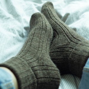 May include: A pair of brown wool socks with a ribbed texture, lying on a white and blue striped bed sheet.