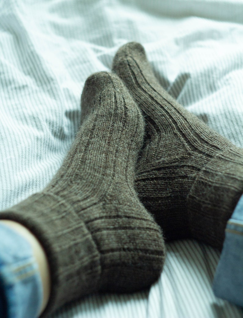 May include: A pair of brown wool socks with a ribbed texture, lying on a white and blue striped bed sheet.