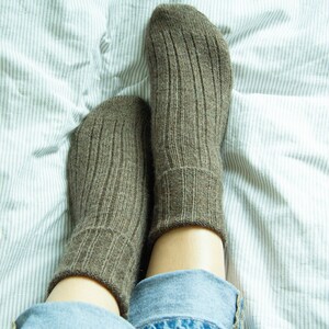 May include: A pair of brown ribbed socks on a white and gray striped bed sheet. The socks are made of a soft, comfortable material and are perfect for keeping your feet warm.