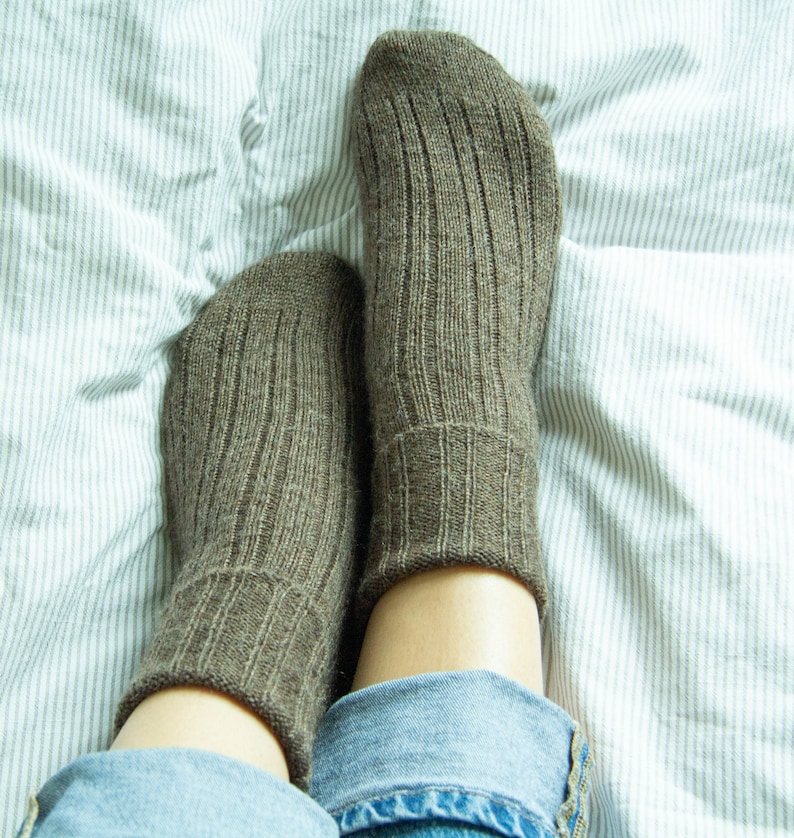 May include: A pair of brown ribbed socks on a white and gray striped bed sheet. The socks are made of a soft, comfortable material and are perfect for keeping your feet warm.