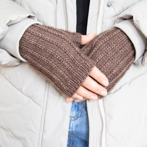 Może przedstawiać: Brązowe dzianinowe rękawiczki bez palców z prążkowanym wzorem. Rękawiczki wykonane są z miękkiego, ciepłego materiału, idealnego na zimną pogodę. Rękawiczki pokazano na tle jasnoszarej kurtki i niebieskich dżinsów.