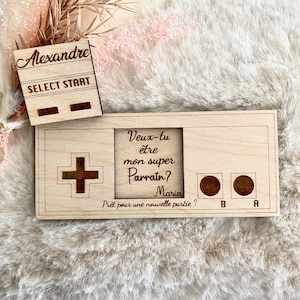 May include: Wooden game controller-shaped plaque with the text "Veux-tu être mon super Parrain? Maria Prêt pour une nouvelle partie?" and "B" and "A" buttons. A separate wooden piece reads "Alexandre SELECT START".