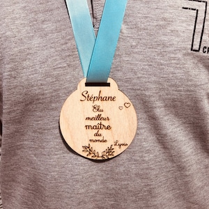 May include: A wooden medal with a blue ribbon, engraved with the text "Stephane Elu meilleur maitre du monde Lyvia".