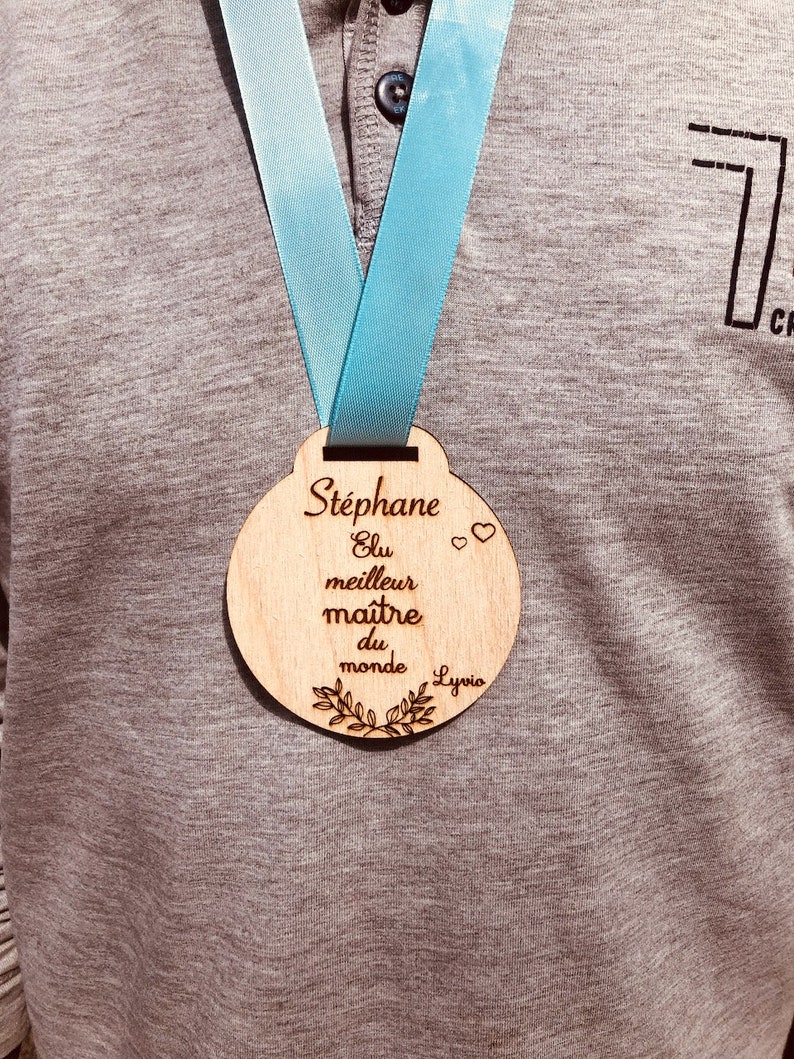 May include: A wooden medal with a blue ribbon, engraved with the text "Stephane Elu meilleur maitre du monde Lyvia".