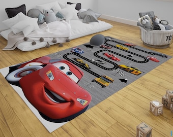 May include: A red race car rug with a black race track and other cars. The rug is on a wooden floor with alphabet blocks and a grey couch in the background.