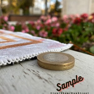 May include: A close-up of a gold-colored coin with a design on it. The coin is sitting on a white wooden surface. The coin is in focus, while the background is blurred. The text "Sample Etsy/Shop/RugStreet" is visible in the bottom right corner of the image.