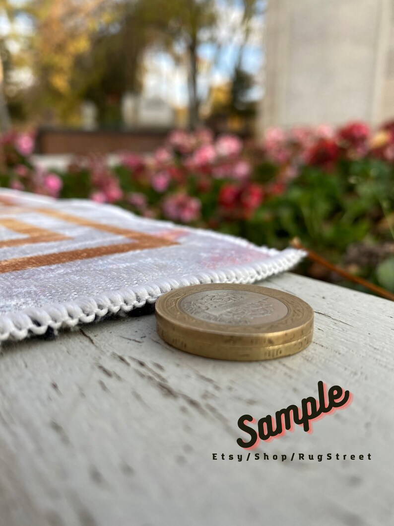 May include: A close-up of a gold-colored coin with a design on it. The coin is sitting on a white wooden surface. The coin is in focus, while the background is blurred. The text "Sample Etsy/Shop/RugStreet" is visible in the bottom right corner of the image.