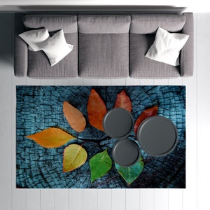 May include: A blue and brown area rug with a wood grain pattern and colorful leaf designs. Three black round coasters are placed on the rug.