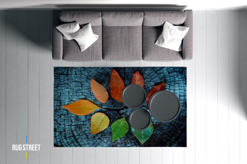 May include: A blue and brown area rug with a wood grain pattern and colorful leaf designs. Three black round coasters are placed on the rug.