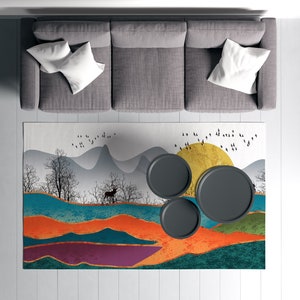 May include: A gray sectional sofa with white pillows sits on a white wood floor. A colorful rug with a mountain and sun design is placed in front of the sofa. Three black round coffee tables are on the rug.