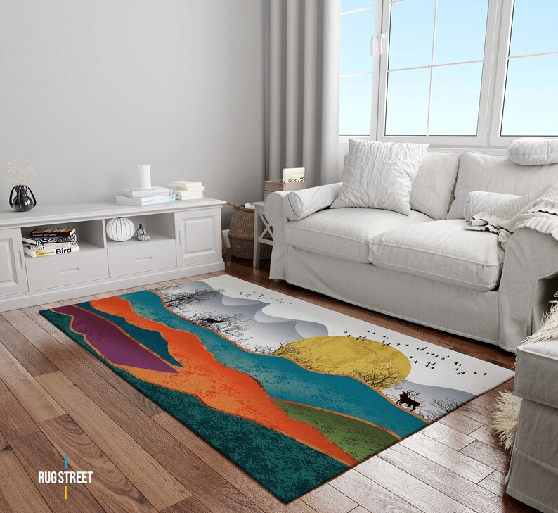 May include: Abstract area rug with a colorful landscape design featuring a deer, trees, and a sun. The rug has shades of teal, orange, purple, and gold.
