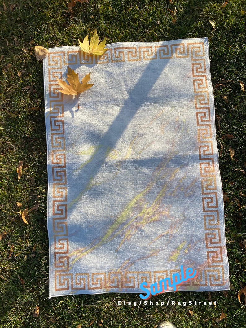 May include: A white rug with a brown Greek key border. The rug has a subtle, light-colored pattern and is lying on a bed of green grass. The text "Sample Etsy/Shop/RugStreet" is visible in the bottom right corner.