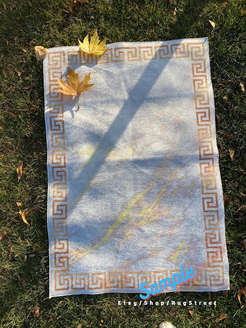May include: A white rug with a brown Greek key border. The rug has a subtle, light-colored pattern and is lying on a bed of green grass. The text "Sample Etsy/Shop/RugStreet" is visible in the bottom right corner.