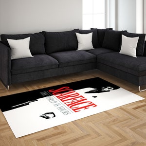 May include: A white and black area rug with a red and white graphic of a man in a suit with the text "Scarface The World Is Yours".