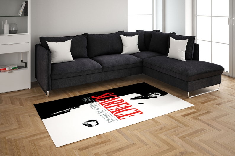 May include: A white and black area rug with a red and white graphic of a man in a suit with the text "Scarface The World Is Yours".