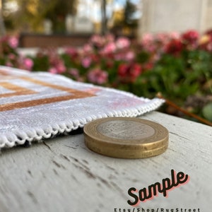 May include: A close-up of a gold-colored coin with a design on it. The coin is sitting on a white wooden surface. The coin is in focus, while the background is blurred. The text "Sample Etsy/Shop/RugStreet" is visible in the bottom right corner of the image.