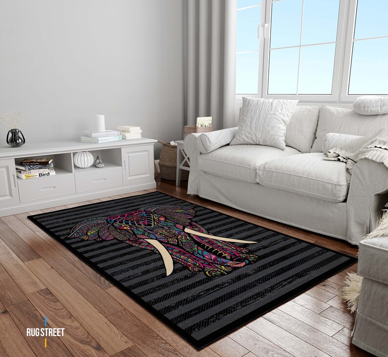 May include: A black and white striped rug with a colorful elephant design. The elephant has pink, blue, green, and yellow details. The rug is on a wooden floor in a living room setting.