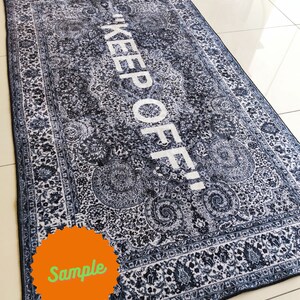 May include: A black and white patterned rug with the text "KEEP OFF!" in white lettering. The rug has a sample label in the lower left corner.