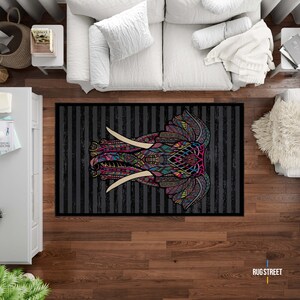 May include: A black and white striped rug with a colorful, patterned elephant head design. The elephant's tusks are white and the design features pink, blue, green, yellow, and orange colors.