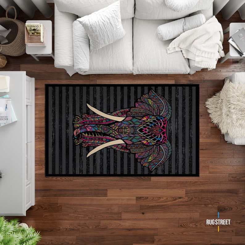 May include: A black and white striped rug with a colorful, patterned elephant head design. The elephant's tusks are white and the design features pink, blue, green, yellow, and orange colors.