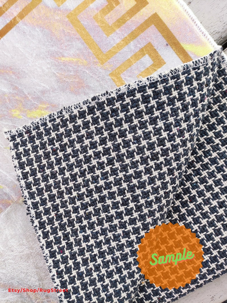 May include: A close-up of a black and white patterned fabric with a gold and white patterned fabric underneath. The fabric has a "Sample" label on it.