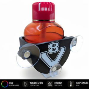 Op de afbeelding: Een auto luchtverfrisser met een rode dop en oranje vloeistof, gehouden in een zwarte houder met een wit "8 V" logo. De houder heeft zuignappen voor montage. De onderkant van de afbeelding heeft pictogrammen met tekst.