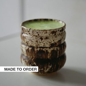 May include: A brown and white ceramic mug with a green liquid inside. The mug has a textured, layered design. The text "MADE TO ORDER" is visible at the bottom of the image.