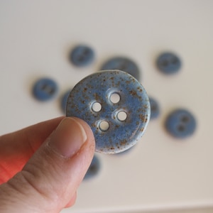 Puede incluir: Un botón de cerámica azul con cinco agujeros y una textura moteada.